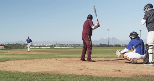Playing baseball, batter in maroon uniform preparing to hit pitch on field
