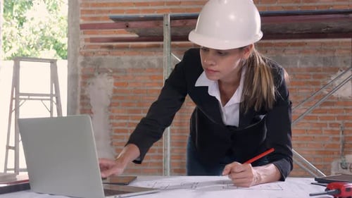Young caucasian architect woman looking laptop and working drawing blueprint for planning.
