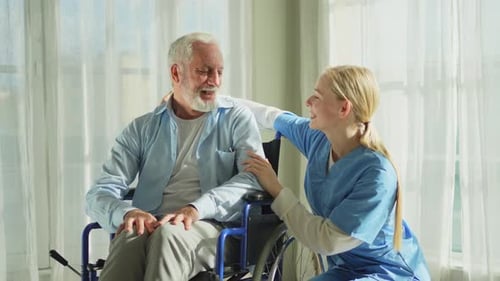 Friendly Young Caregiver Talking with Senior Man in Wheelchair