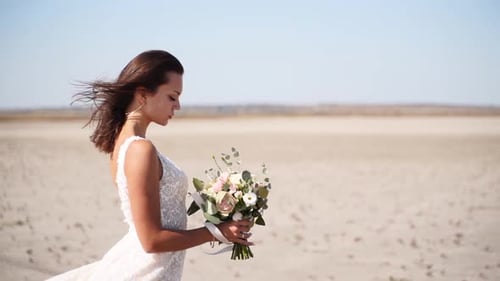 Romantic Bride with Delicate Wedding Bouquet at Desert Landscape Hair of Pretty Woman Blowing in a