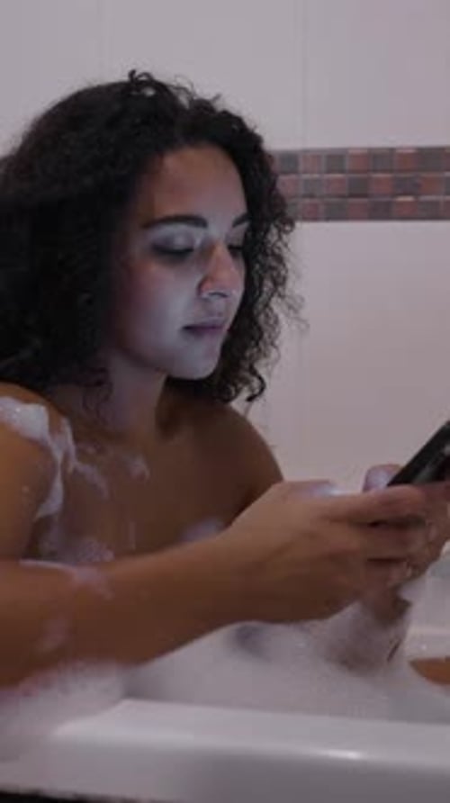 Woman Relaxing in a Bubble Bath with Phone