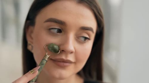 close-up portrait of a young woman massaging her face with a jade roller