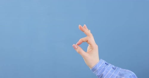 Woman's Hand Making OK Gesture on Blue Background