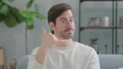 Call Me Gesture by Young Man Sitting on Sofa at Home