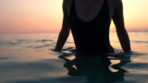 Young beautiful woman walking in the sea at sunset in slow motion paradise