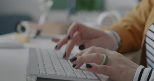 Closeup of Female Hands Typing with Wireless Computer Keyboard While Businesswoman Working at Desk
