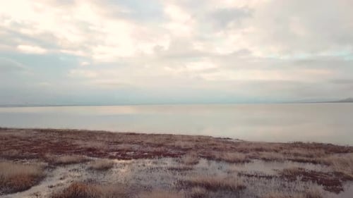 Gliding above a marshy area towards a vast lake with sky reflecting off the water