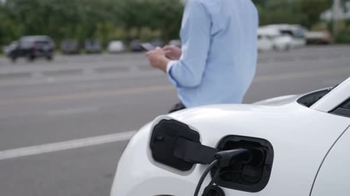 Man Using Phone While Charging Electric Car