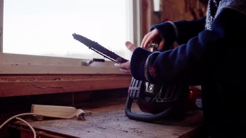 Man Repairing Chainsaw in Workshop by Window