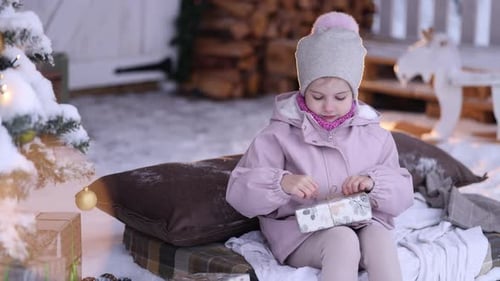 Little Girl Opens Gift on Snowy Christmas Day