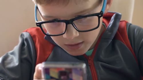 Boy with Glasses Plays on Mobile Phone Indoors