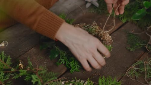 Hands making Christmas wreath in floral workshop, eco friendly Xmas home decor.