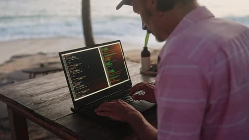 Web Developer Programs at Oceanfront Beach Cafe at Sunset Male Typing Edits Code on Laptop Screen