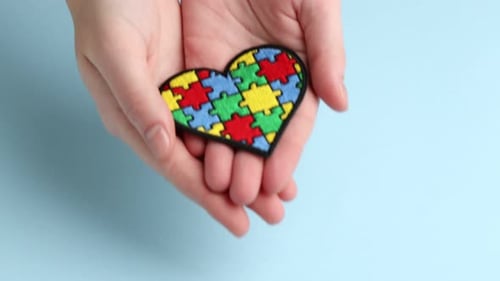 Autism. Woman with heart made of puzzle pieces on light blue background, closeup