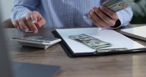 Woman Counting Money and Using Calculator at Desk