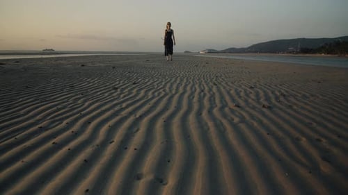 Woman Walking Alone on Rippled Sand Beach at Sunset