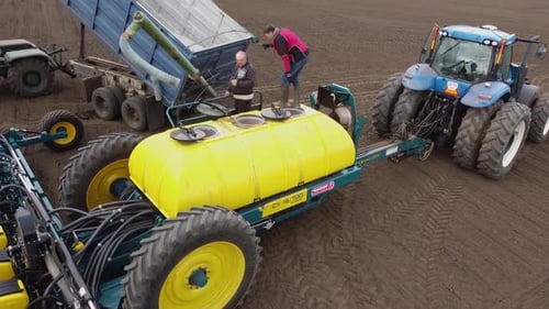 Blue tractor with yellow seeder working on the field in Ukraine OA