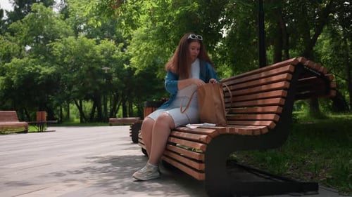 Mujer sentada en un banco del parque devolviendo el material bordado a la bolsa