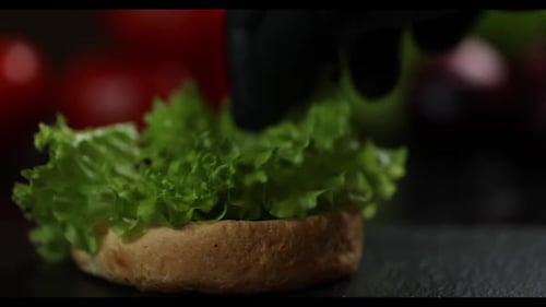 Gloved Hand Places Lettuce Slice on Burger Bun