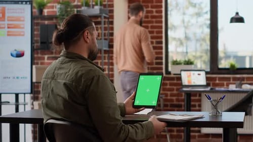 Man at Desk Holding Green Screen Tablet in Office