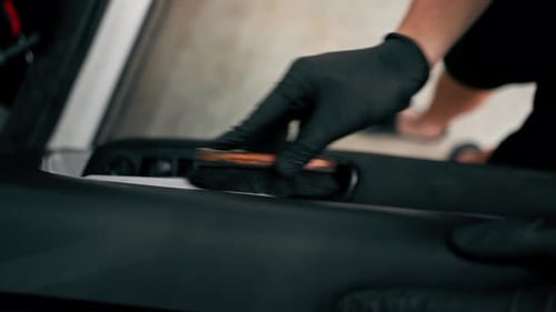 Close-up of a car wash worker using a plastic washing brush while cleaning the door card of a car