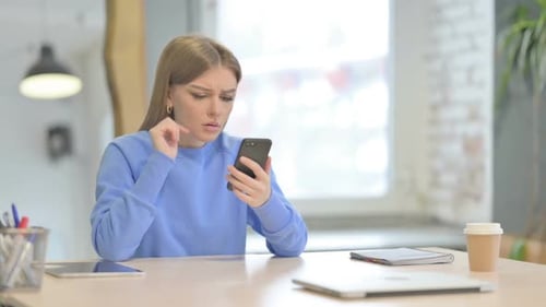 Frustrated Woman Uses Smartphone at Desk Indoors