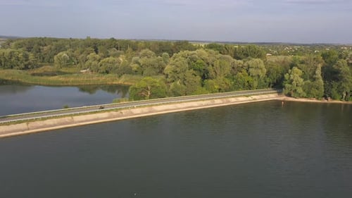 Biker is Driving Motorbike Through Bridge of River on Summer Day