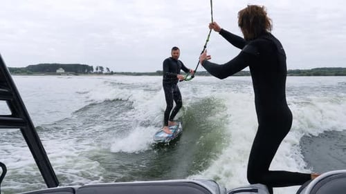 Man Wakesurfing Behind Boat on Lake on Cloudy Day