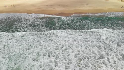 Slow pan-up aerial shot of people relaxing on the sand of the California coastline as the blue water