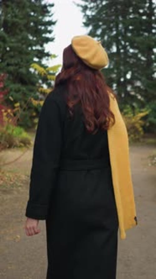 Back View of Young Woman Strolling Through Vibrant Autumn Park in Yellow Beret and Scarf