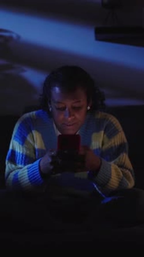 Young Black Girl Chatting on Smart Phone at Night in Living Room Addicted to Technology