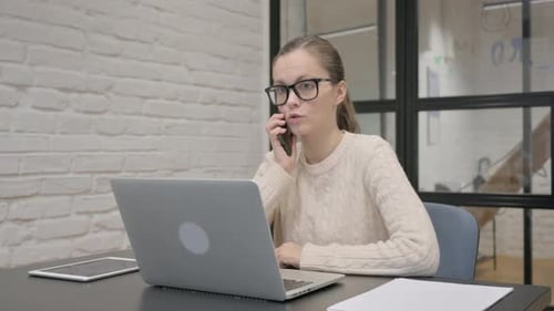 Woman Working at Laptop During Phone Conversation