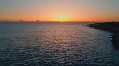 Golden sunset over dark serene ocean waters rippling on the beach at sundown