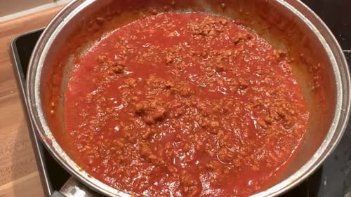 Bolognese sauce with minced meat is cooking in a pan on the stove