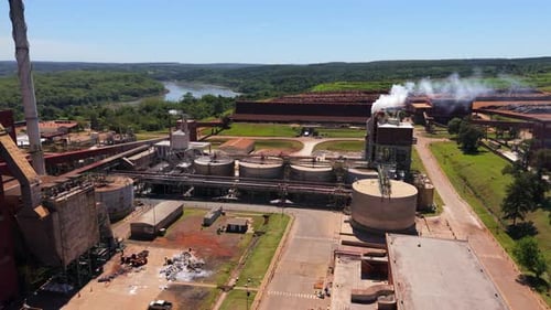 Panoramic drone fly over an industrial paper wood factory mill complex with storage tanks.