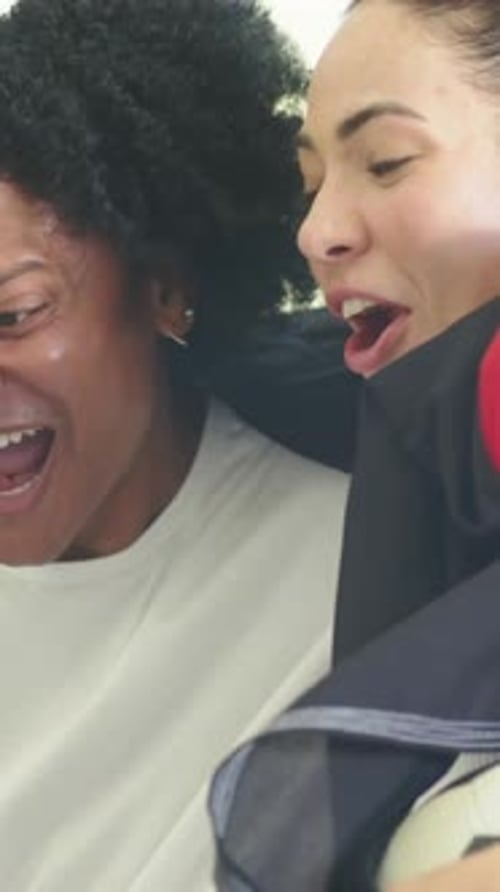 Vertical video: Laughing two women reacting after surprise offscreen in bright room, red jacket