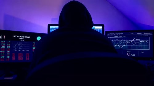 Hooded Figure Analyzing Data on Multiple Screens
