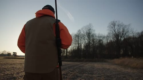 Hunter Walks Through Field At Sunset With Rifle Slow Motion