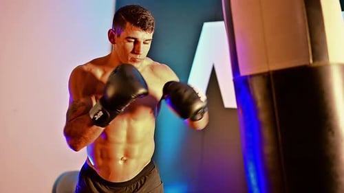 Muscular Man Punches Punching Bag in Gym