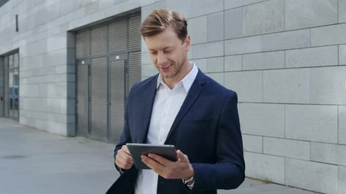 Smiling businessman browsing internet on digital tablet in urban city street