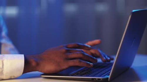 Hands Typing on Laptop in Blue Office at Night