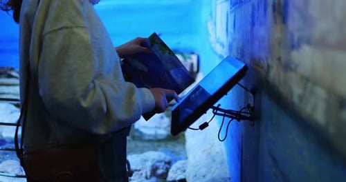 Visitor Stands Against Aquarium and Presses Finger on Interactive Screen