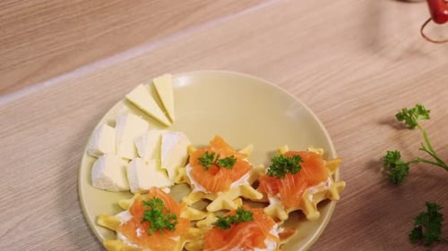 Weibliche Handarbeit beim Arrangieren von Käsestücken auf einem Teller mit herzhaften Waffeln und Lachs, Vorspeisenstyling und