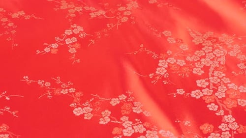 Lustrous red silk rose shade textile fabric background with floral embroidery in oriental style