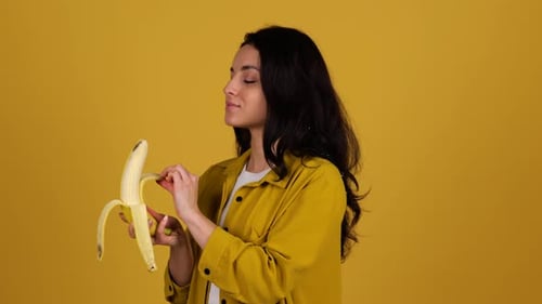 Woman Eats Banana Against Yellow Background