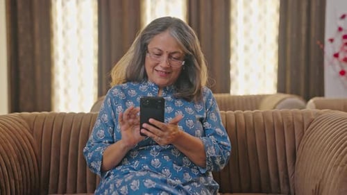 Senior Woman Using Smartphone on Brown Couch Indoors