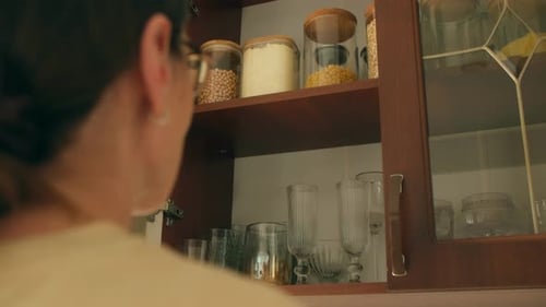Woman Retrieves Clear Container Filled with Cereals From Cupboard