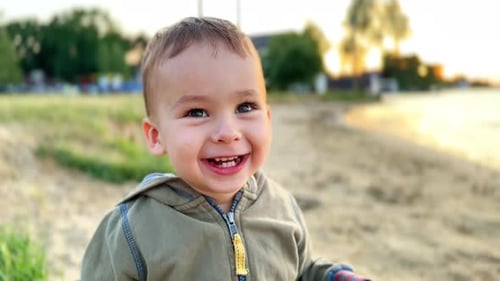 Adorable smiling Caucasian boy on the shore. Curious kid looks into camera. Close up.