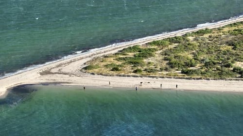 Stationary drone shot of fisherman fishing off a sand bank peninsula. Shot on a zoom lens. Shot off