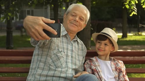 Grandfather and Grandson Taking Selfie on Park Bench
